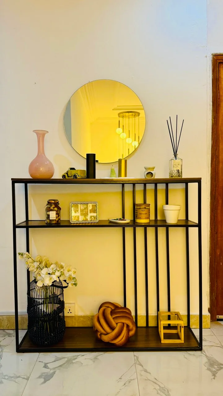 Black metal console table with open shelves and a round mirror